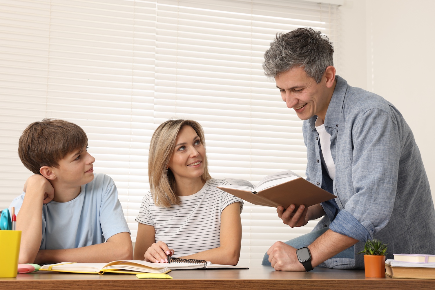 Smiling parents helping their son with homework at table indoors Parent's helping a child with schoolwork.